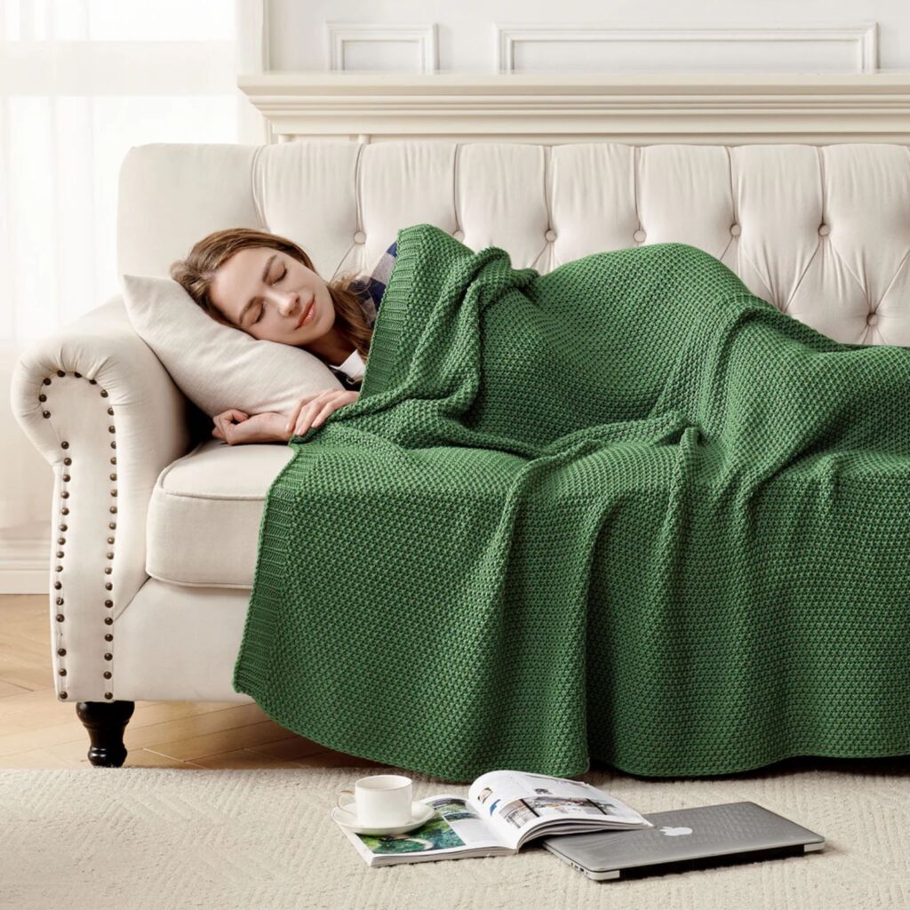 Woman resting on a sofa covered with a chunky green knit throw blanket.