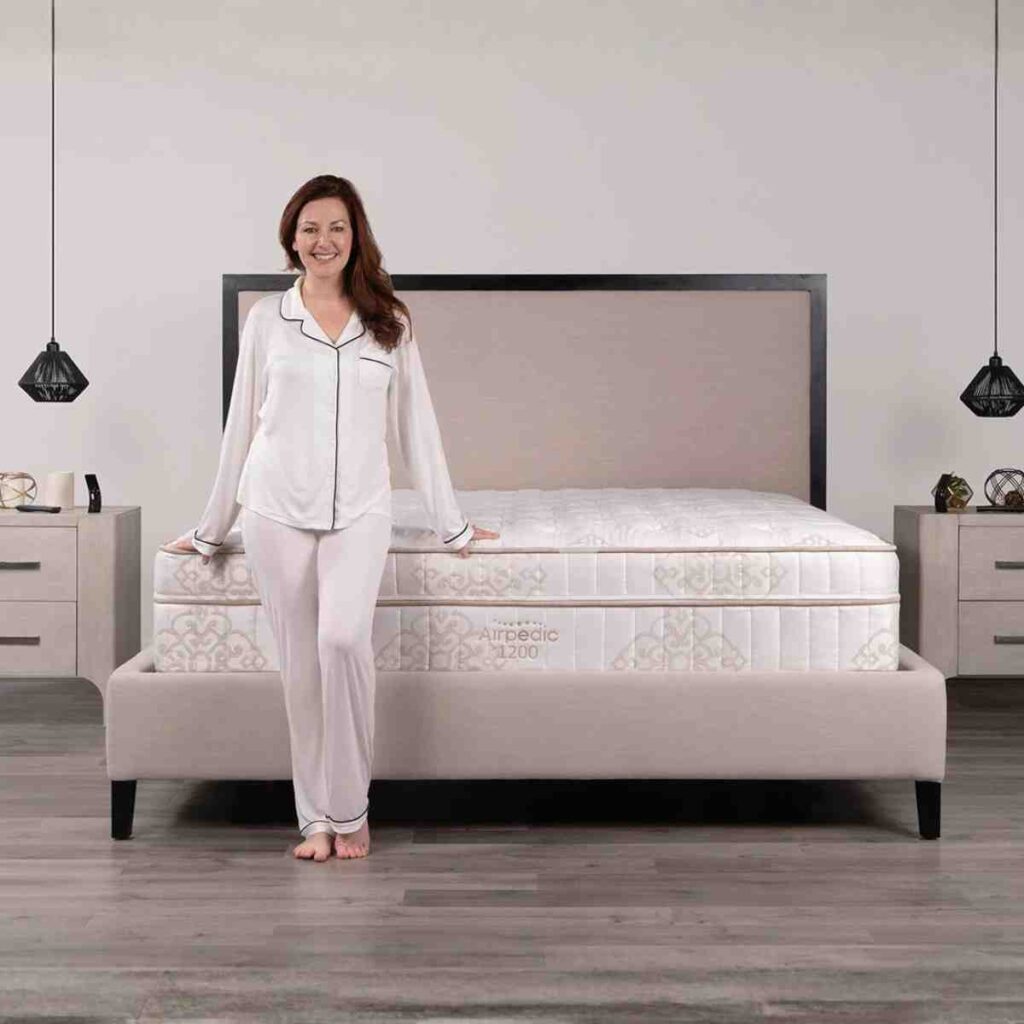 Woman standing next to the Airpedic 1200 flagship mattress, showcasing the ultra-premium quilted top and 15-inch profile.