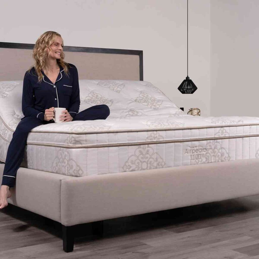 A woman sitting up in an Airpedic premium adjustable bed with a cup, showcasing the versatile lifestyle comfort of an air-supported mattress.