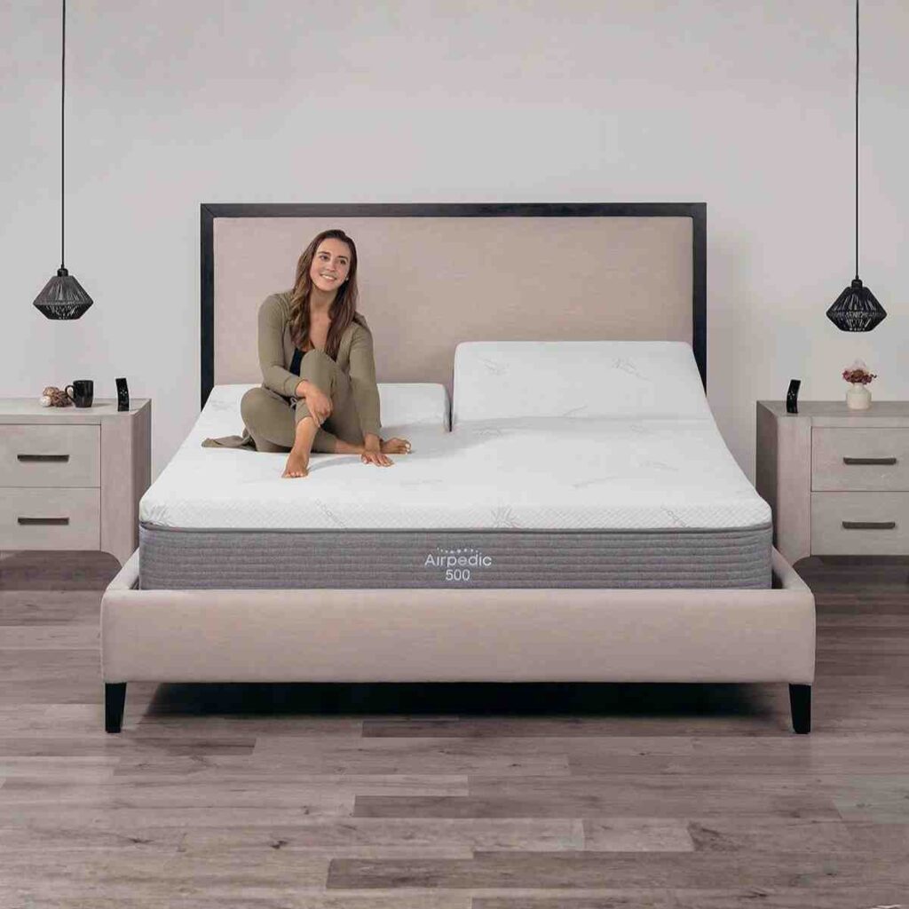 An Airpedic mattress being adjusted via a smart tablet in a grey modern bedroom to provide instant lower back pain relief.