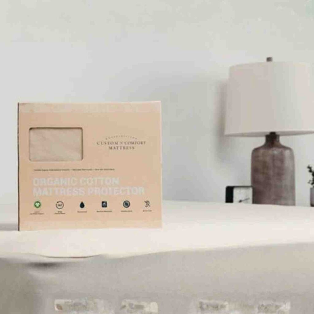 An Airpedic mattress protector in its original packaging sitting on the corner of a bed in a bright bedroom.