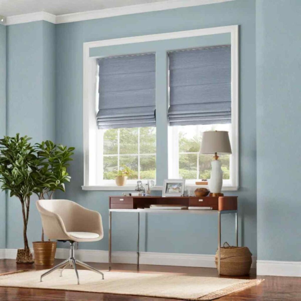 A soft blue tailored Roman shade installed in a bright home office, featuring crisp horizontal folds and a cordless design.