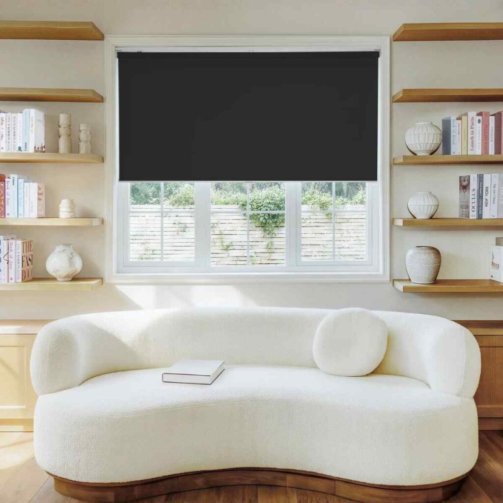 A modern white bouclé sofa positioned under a sleek Joydeco black blockout roller shade in a bright, minimalist living room setting.