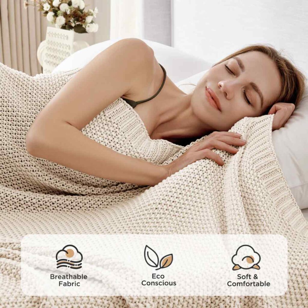 A woman resting under a beige Joydeco chunky knit throw blanket in a cozy bedroom.