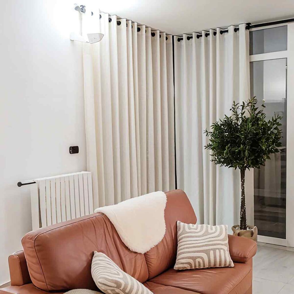 Floor-to-ceiling Joydeco cream blackout curtains in a warm, neutral living room featuring a tan leather sofa and soft ambient lighting.