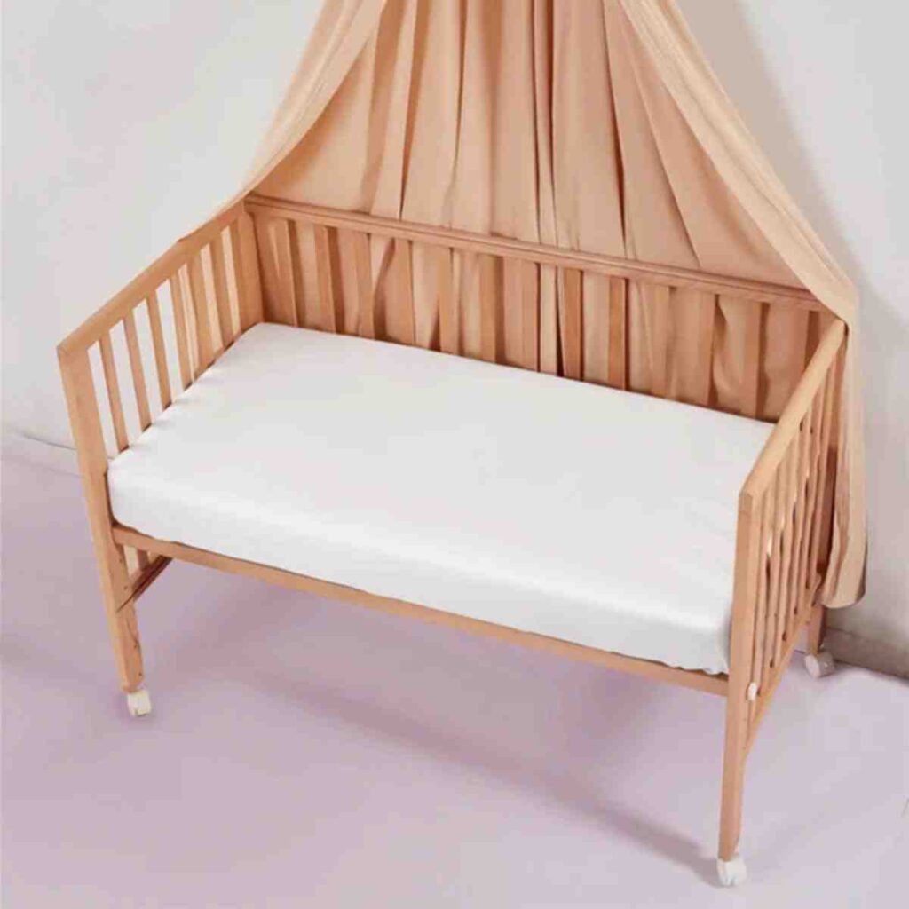 A white Promeed silk sheet fitted onto a wooden baby crib mattress.
