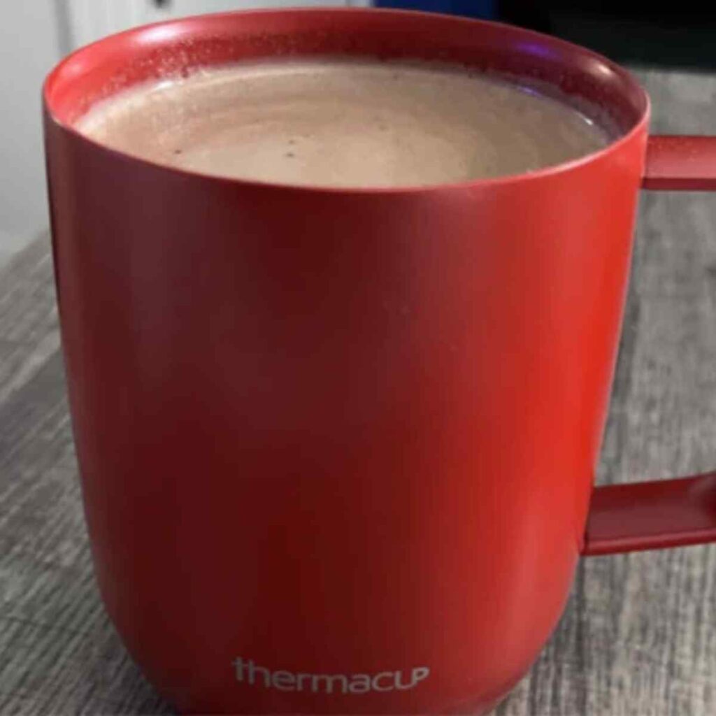 A close-up view of a vibrant red Thermacup filled with coffee, emphasizing its smooth ceramic-like texture and rich color.