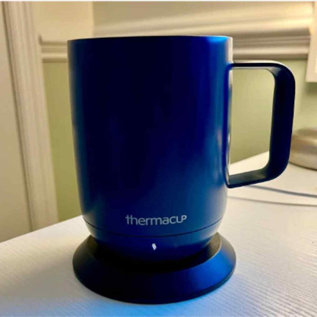 A royal blue Thermacup smart mug sitting on its black circular charging base, highlighting its sleek metallic finish and modern design.