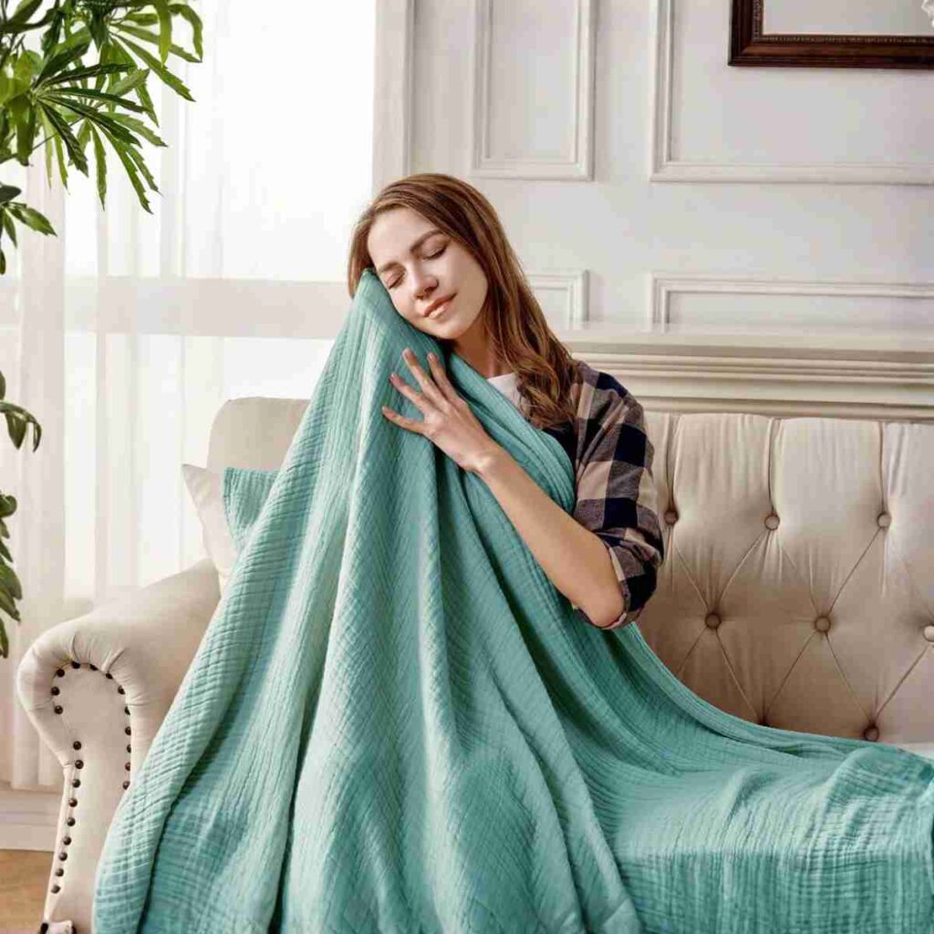 Shop Joydeco Sage Muslin Throw Joydeco Sage Green 100% Cotton Muslin Throw Blanket draped on a sofa.
