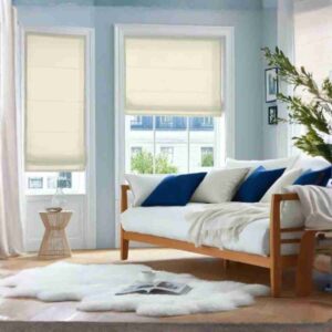 Two elegant beige semi blackout roman shades installed in a bright coastal-style living room with a white sofa and blue accent pillows.