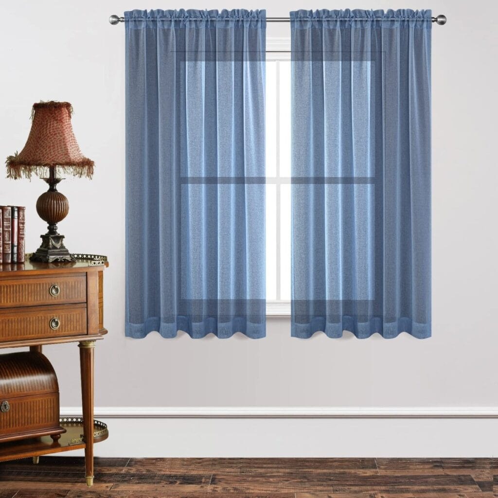 A modern well-lit home interior showing functional sheer curtains navy blue mounted clean over a residential glass window frame.