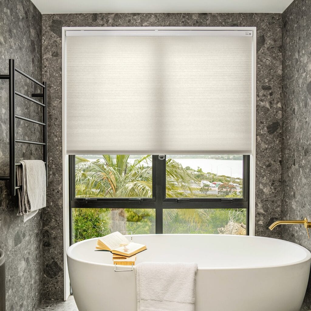 Beautifully arranged bathroom displaying a window half covered with a cellular light filtering shade grey.