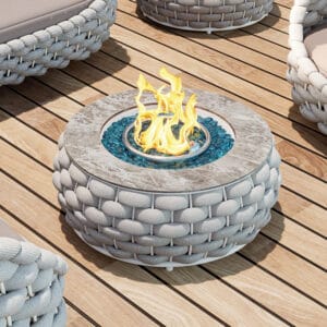 Round outdoor propane fire pit with hand-woven rattan and marble-look top for outdoor gatherings.